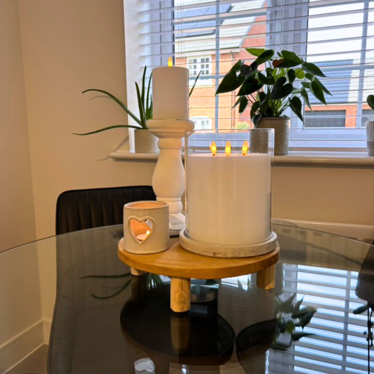 Decorative setup of a large hurrican candle holder with candles and plants on a table near a window