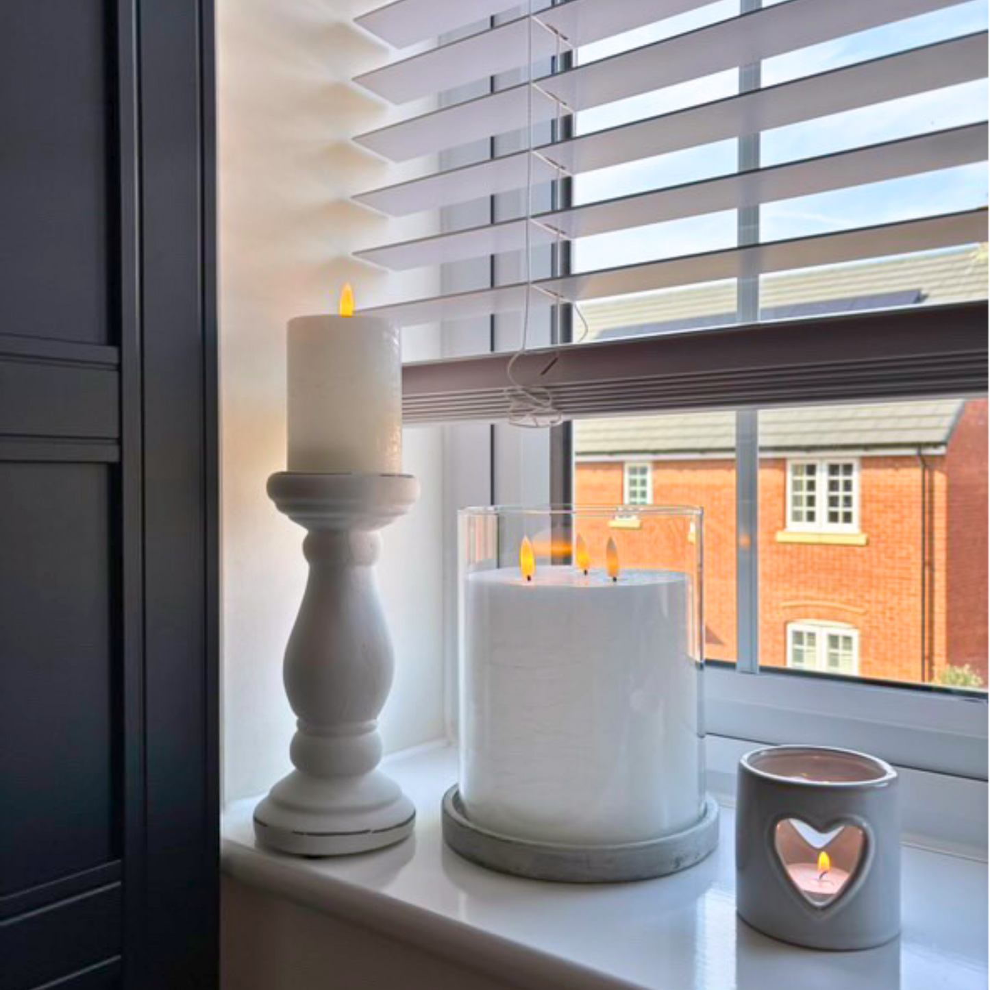 Stone-based large hurricane candle holder styled with candles on a windowsill with a view of a house outside
