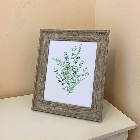 Framed artwork with green leaf design on a white surface against a beige wall
